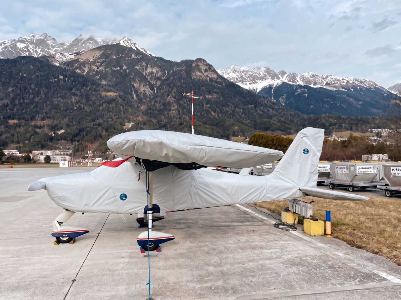 Motorflugzeug mit Jaxida Allwetter-Cover auf dem Flugplatz vor den Alpen
