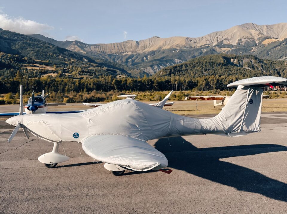 Ultraleichtflugzeug mit passgenauer weißer Jaxida Flugzeugabdeckung vor Bergkulisse